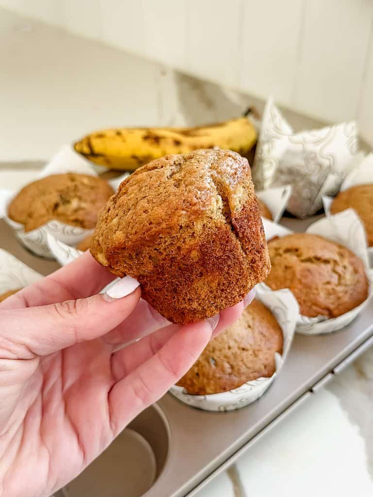 a hand holding one of the banana bread muffins