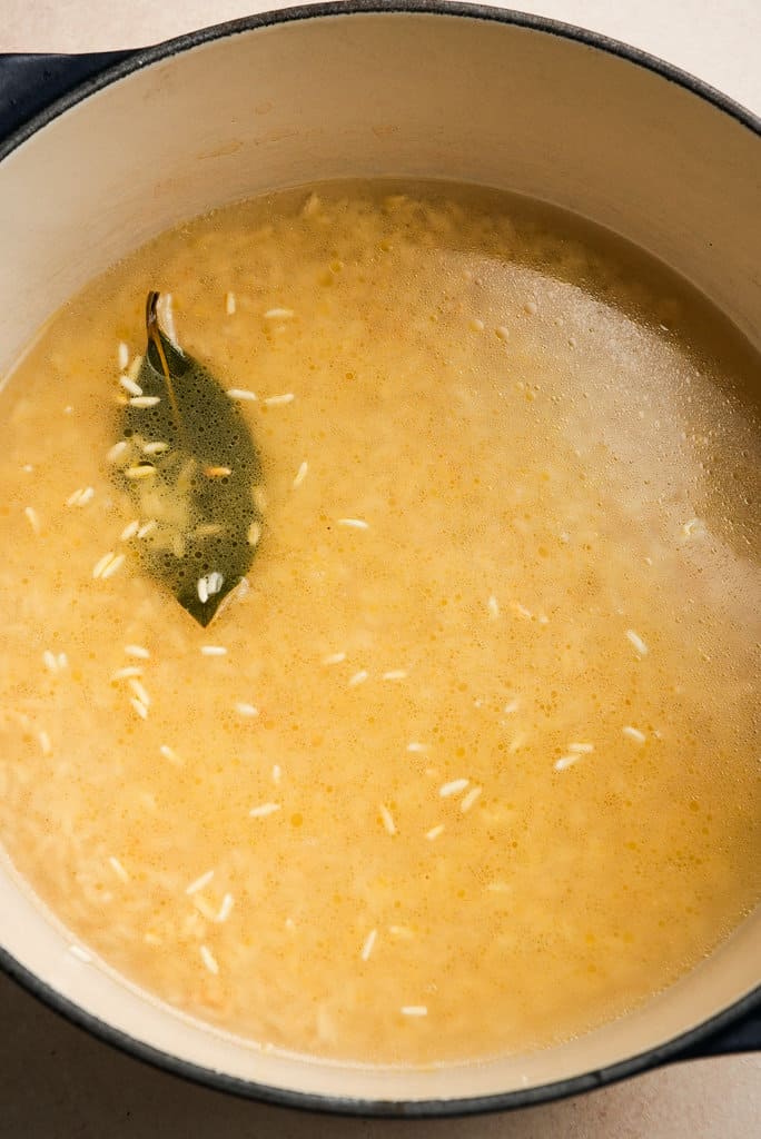 a pot of chicken broth, water, and rice with a bay leaf