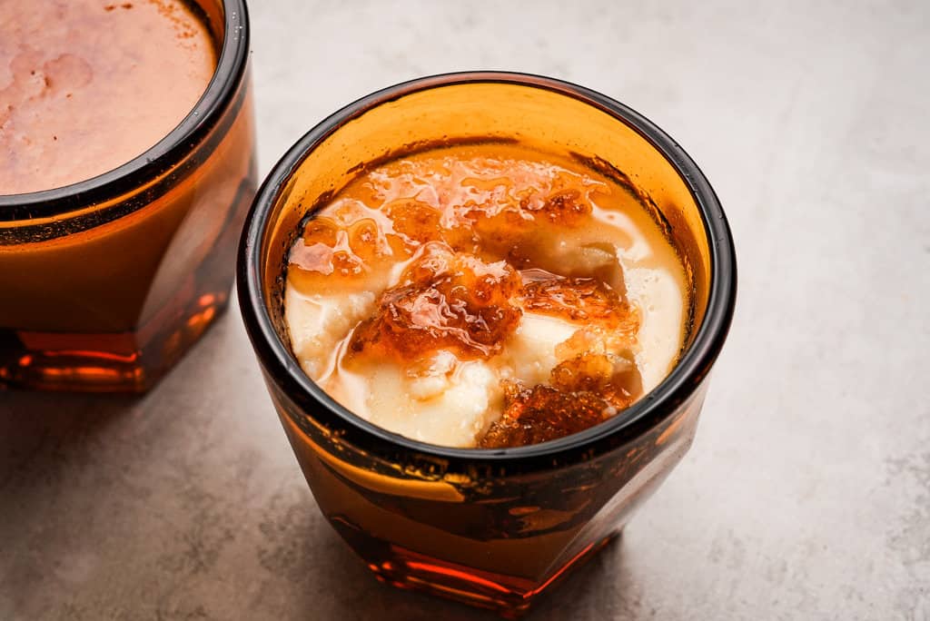 two jars of panna cotta with one jar in focus, with brûlée topping cracked to reveal smooth cream underneath