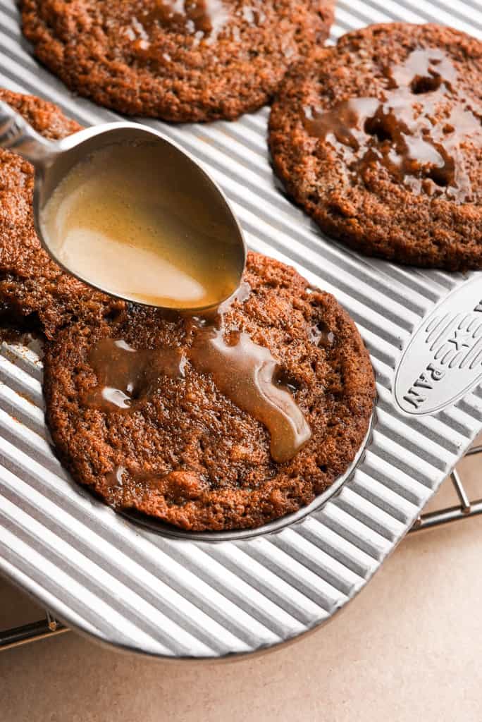 a spoon pouring toffee sauce over sticky toffee pudding while they're still in the muffin tin