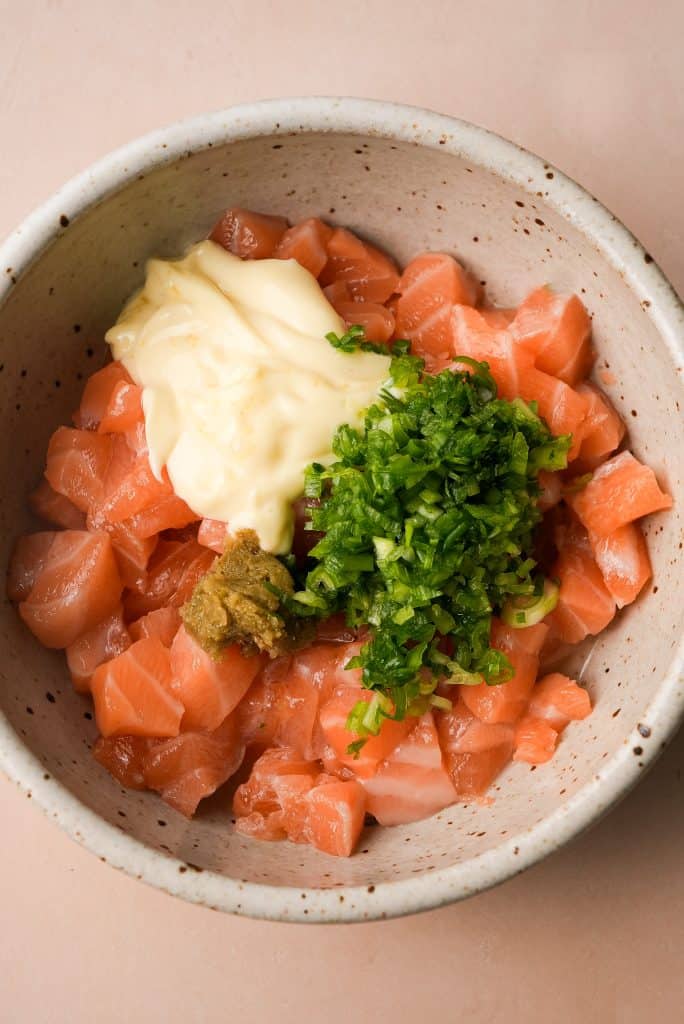 sushi-grade salmon topped with seasoning ingredients, prior to mixing
